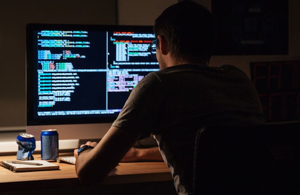 51967686 - back view of modern programmer sitting and writing code in dark room
